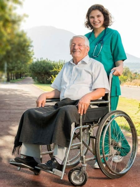 Caregiver assisting a senior man in a wheelchair outdoors