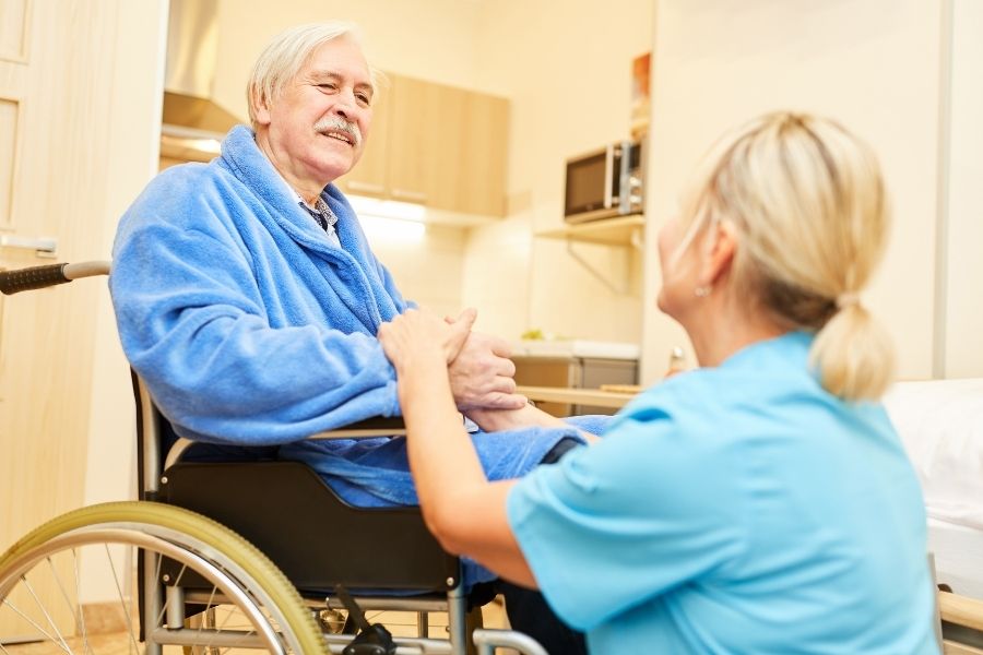 Caregiver taking care of senior man who is on wheel chair and had surgery