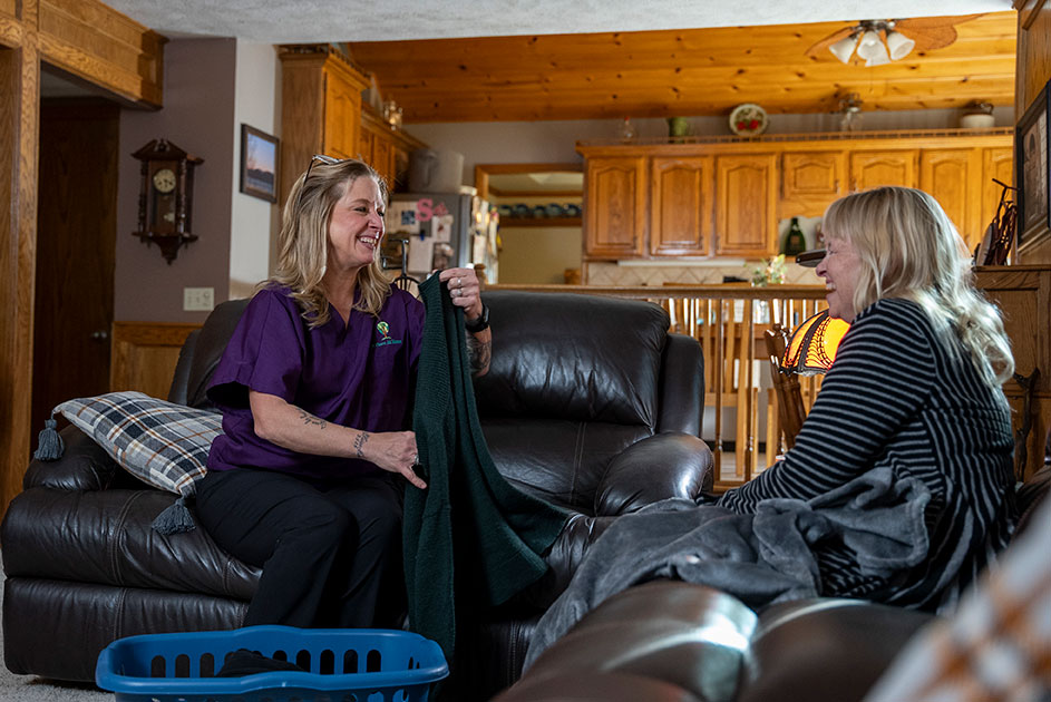 Caregiver folding elderly woman's laundry while they have a conversation.