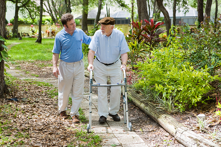 Caregiver walking in garden with elderly man.