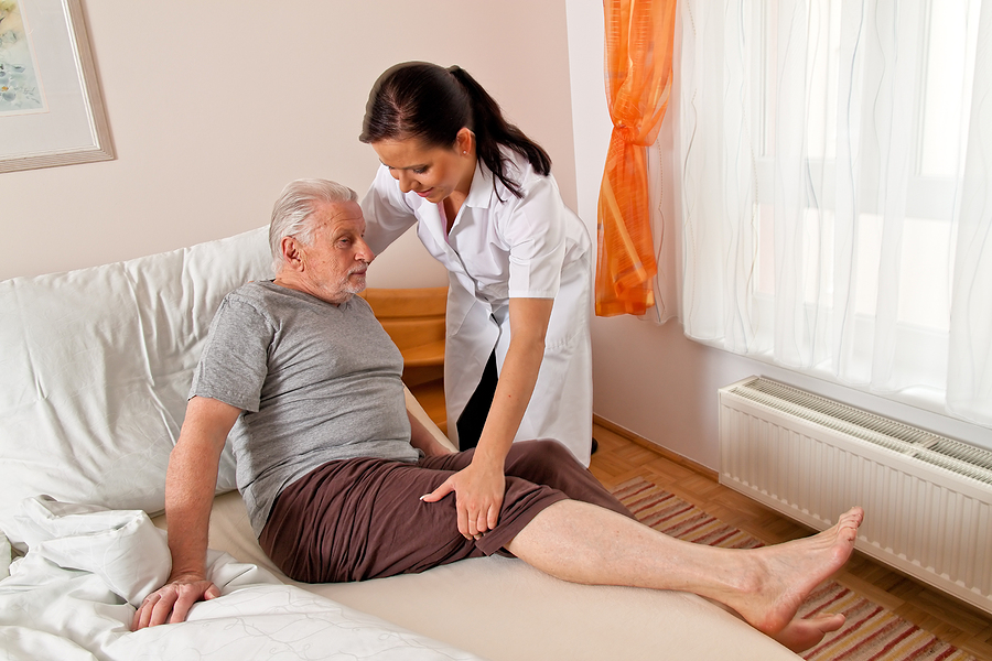 Caregiver helping elderly man out of bed.