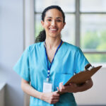 Smiling Medical Professional in Scrubs Holding a Clipboard in Hospital Setting