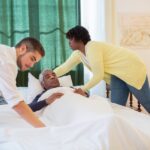 Two caregivers helping an elderly man get in bed