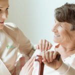 Happy elder lady holding a wooden walking stick and talking to her young caregiver