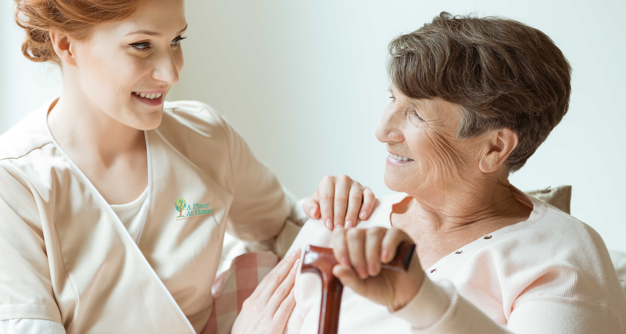 Happy elder lady holding a wooden walking stick and talking to her young caregiver