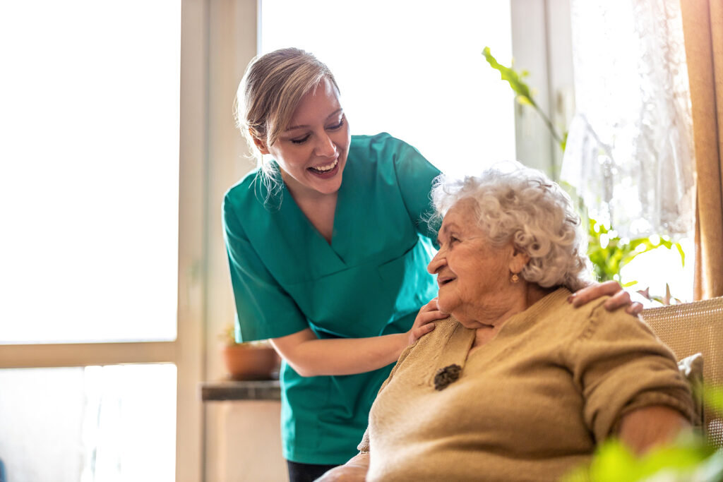 Smiling caregiver holding onto elderly woman's shoulder