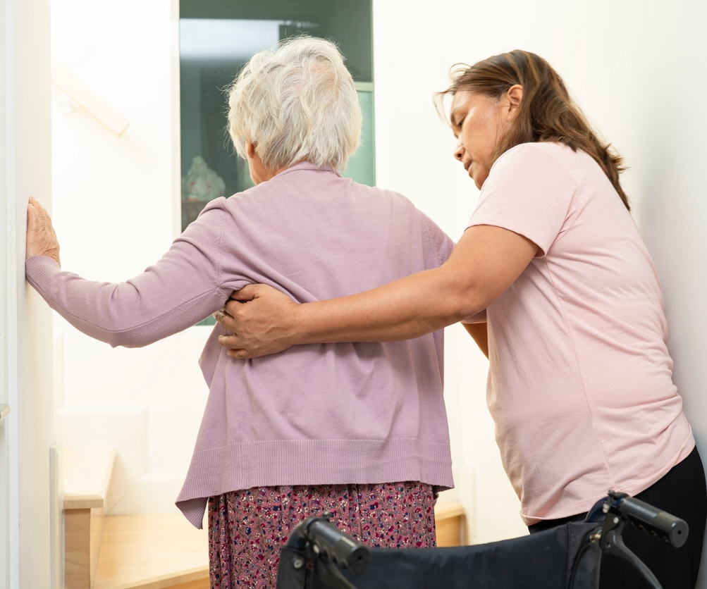 Caregiver helping elderly old woman sitting wheelchair support up the stairs in home.