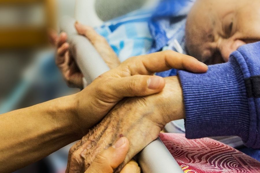 Caregiver holding a sleeping senior's hand during overnight care in Los Alamitos, CA