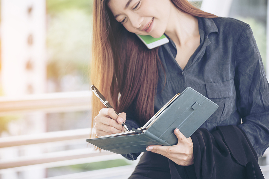 Young woman on phone taking notes in notepad
