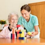 Dementia-Caregiver-Assisting-Senior-woman-with-a-mind-game-to-keep-her-active