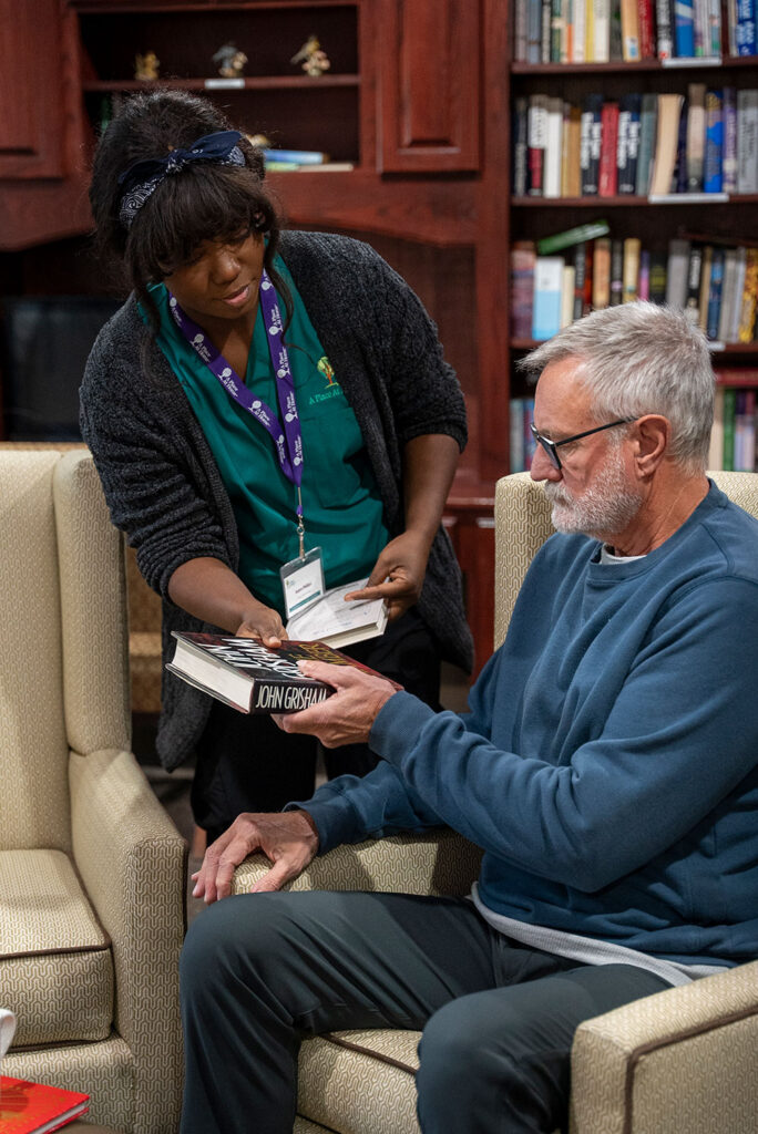 Caregiver handing elderly man a book in the library