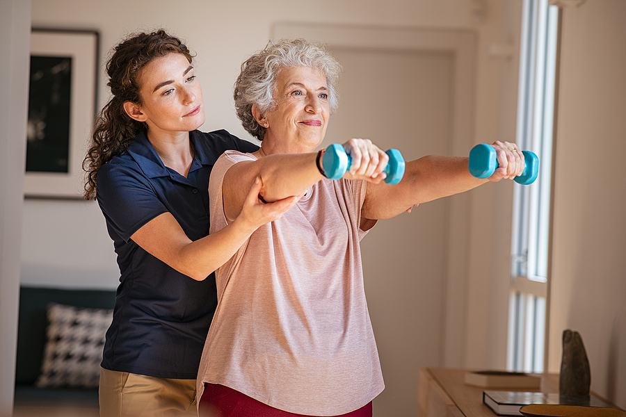 Caregiver helping elderly woman lift weights