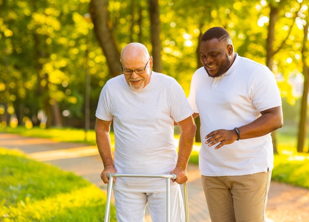Home healthcare worker walking with elderly man in the park.