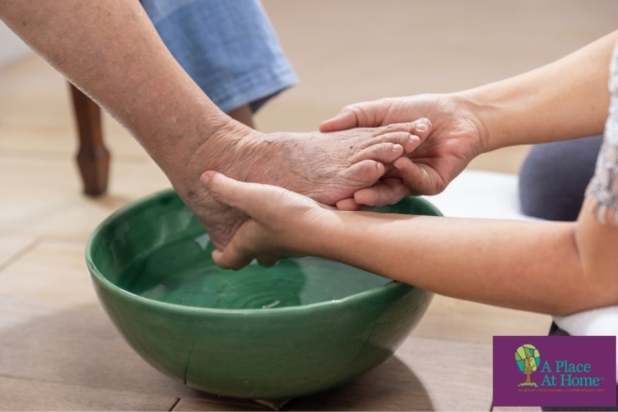 Caregiver applying warm compress and helping senior soak legs in warm water for cramp relief.