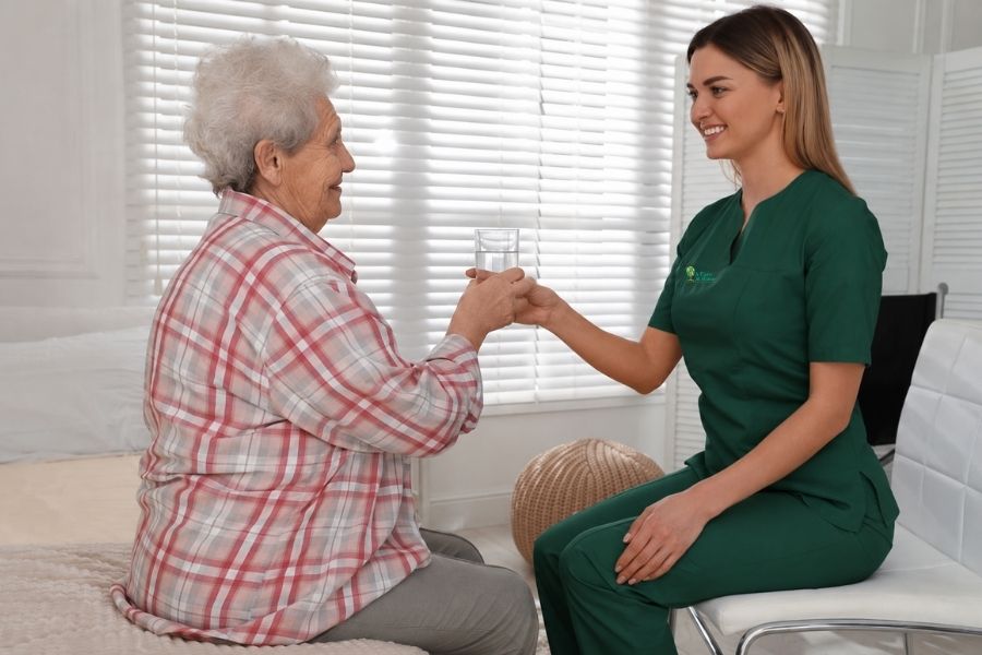 A Place at Home Caregiver giving a glass of water to senior woman in hand
