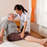 Caregiver helping elderly man out of bed.