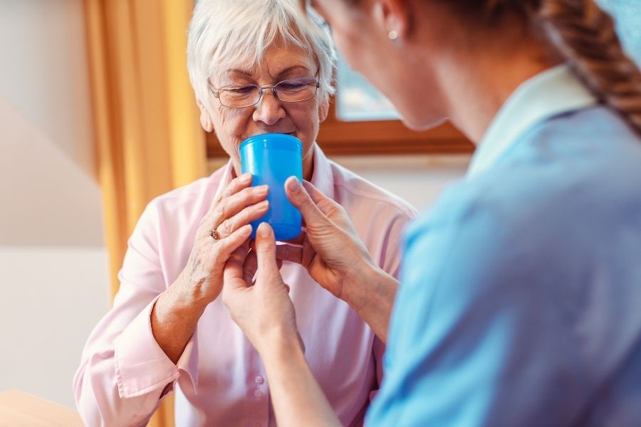 caregiver giving water to senior woman to prevent dehydration caregiver giving water to senior woman to prevent dehydration