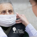 A caregiver helping place a mask on a senior.