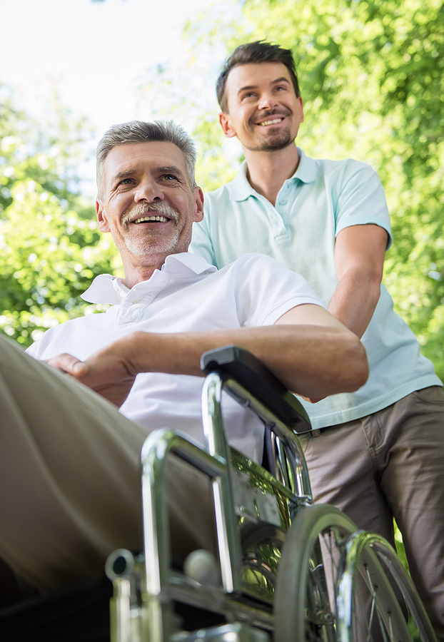 Caregiver pushing elderly man in wheelchair outdoors.