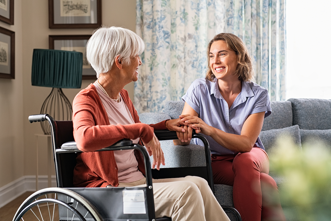Elderly woman in wheelchair talking to careigver in living toom
