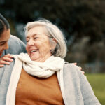 Caregiver helping woman with disability in park for support, trust and care in retirement. Nurse talking to happy senior patient in wheelchair for rehabilitation, therapy and conversation in garden