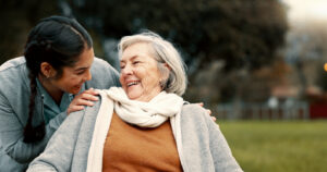 Caregiver helping woman with disability in park for support, trust and care in retirement. Nurse talking to happy senior patient in wheelchair for rehabilitation, therapy and conversation in garden