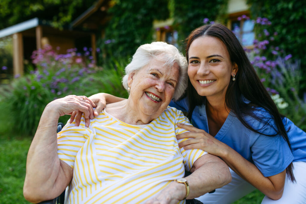 Portrait of caregiver taking of lovely elderly patient in wheelchair.